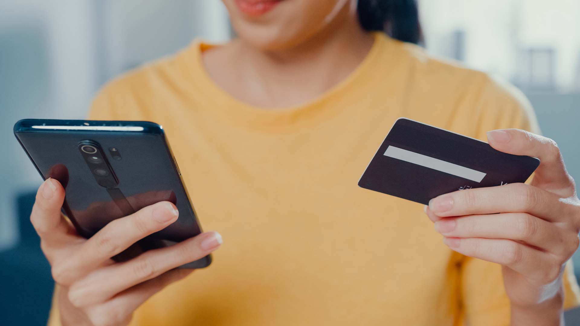 The photo shows a woman using her credit card to make purchases on her phone. 